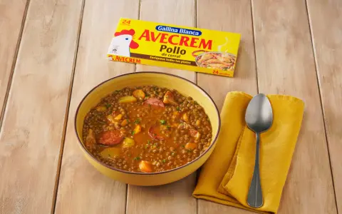 Un tazón de lentejas estofadas con chorizo y patatas, junto a un paquete de Avecrem Pollo.