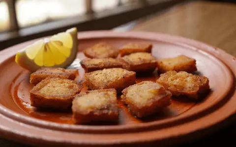 Deliciosos trozos de bacalao rebozado, dorados y crujientes, servidos en un plato de barro con una rodaja de limón.