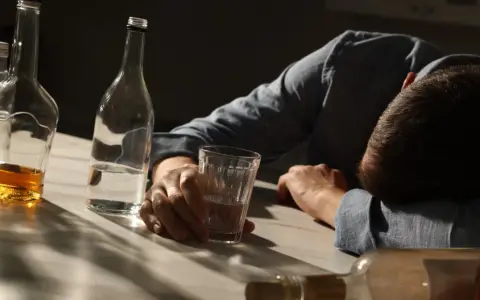 Mężczyzna śpi na stole, otoczony butelkami alkoholu. To obraz, który mógłby ilustrować straszne historie alkoholików, opowiadające o samotności i utracie kontroli.