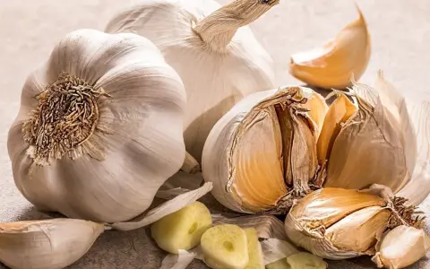 Mehrere Knoblauchzehen und ganze Knoblauchköpfe liegen auf einer hellen Oberfläche. Tipps zur Lagerung von Knoblauch.