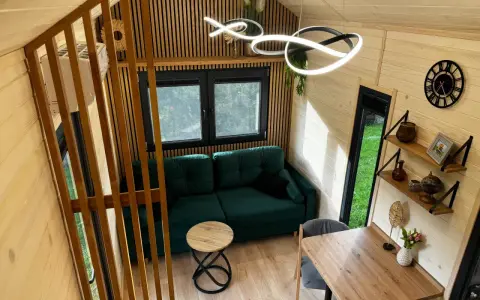 Przytulne wnętrze tiny house Polska: zielona kanapa, drewniane meble i nowoczesne oświetlenie. Idealne miejsce na relaks.