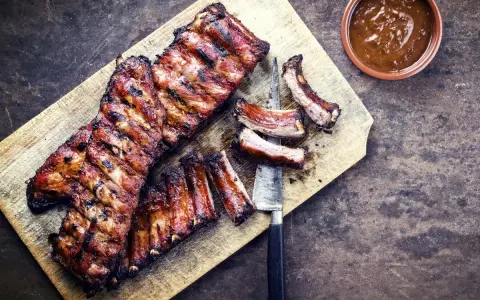 Soczyste żeberka w miodzie, grillowane do perfekcji, leżą na desce obok sosu.