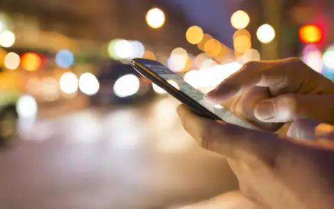 Hände bedienen ein Smartphone im nächtlichen Stadtverkehr. Tipps, um das iPhone schneller machen, sind hier vielleicht gesucht.