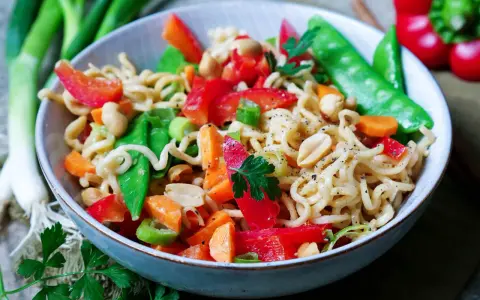 Bunter mie nudelsalat mit Erdnüssen, Zuckerschoten, Karotten und Paprika, garniert mit Petersilie.