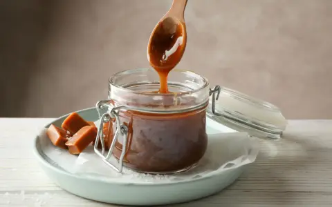 En träsked droppar krämig kolasås ner i en burk. Perfekt för ditt kolasås recept!