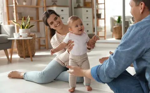 Rodzice zachęcają dziecko do pierwszych kroków. Uśmiechnięta mama i tata z otwartymi ramionami motywują malucha do chodzenia.