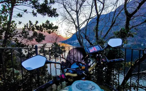Manubrio moto con vista panoramica sul Lago di Como al tramonto. Un invito a esplorare i punti panoramici in moto.