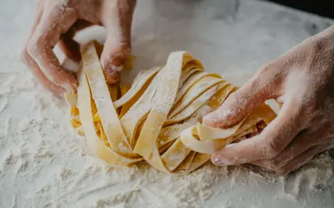 Mani infarinate lavorano un nido di tagliatelle fatte in casa, pronte per essere cucinate.