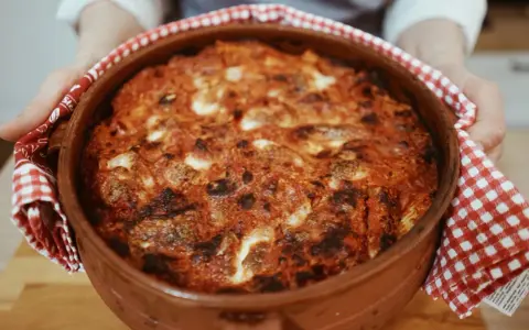 Un invitante pasta al forno ricetta della nonna, appena sfornata in una terracotta, con crosticina dorata e ripieno filante.