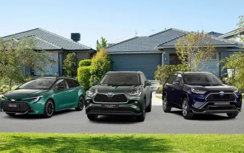 Trzy modele Toyota SUV: zielony kombi, ciemnozielony Highlander Hybrid i granatowy RAV4 Plug-in Hybrid, zaparkowane przed domami.