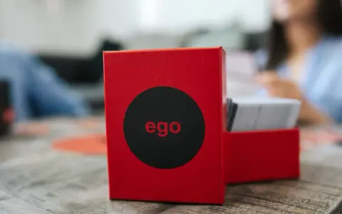 Czerwone pudełko gry "ego" z czarnym kołem i napisem "ego" w środku. Obok stos kart. Czas na ego gold pytania!