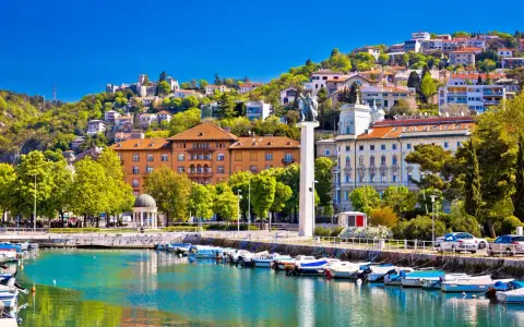 Malowniczy port w Chorwacji z łodziami przycumowanymi do nabrzeża. W tle widać wzgórze z zabudowaniami i zamek.