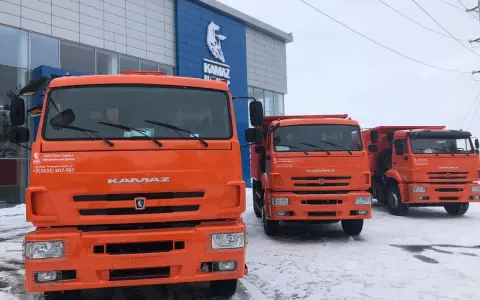 Trzy pomarańczowe, rosyjskie ciężarówki KAMAZ stoją przed budynkiem dealera.