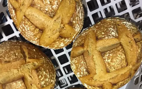 Trois pains au levain dorés, prêts pour la cuisson sur sole. Leurs croûtes craquelées et leurs incisions en croix promettent une texture parfaite.