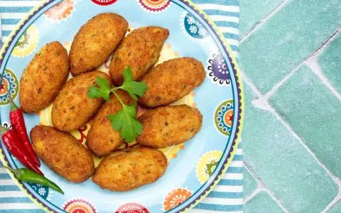 Croquetas doradas en un plato decorado con pimientos y perejil.