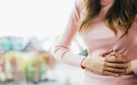 Kobieta trzyma się za brzuch, odczuwając dyskomfort. Wzdęty brzuch rano to częsty problem.
