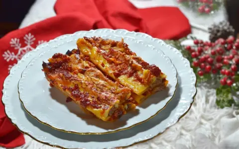 Due cannelloni di carne fumanti, ricoperti di sugo rosso e formaggio filante, serviti su un piatto bianco con bordo dorato, pronti per essere gustati.