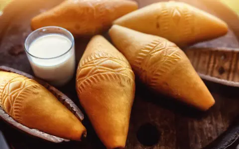 Kilka oscypków z ozdobnymi wzorami i szklanka mleka na drewnianym tle.