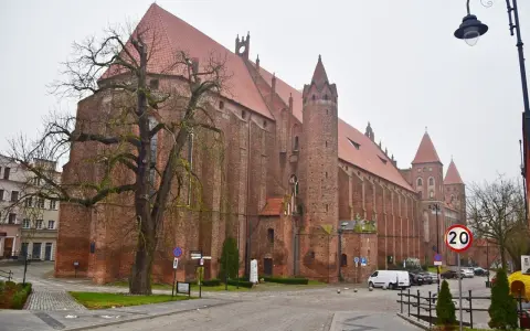 Imponująca katedra w Kwidzynie, z cegły, z charakterystycznymi wieżami i czerwonym dachem, otoczona drzewami i budynkami.