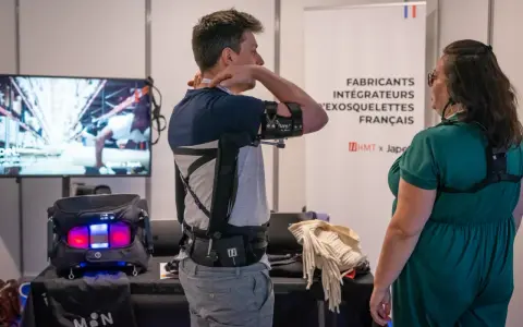 Un homme teste un exosquelette pour le bras, une technologie d'assistance pour le handicap. Une femme observe.