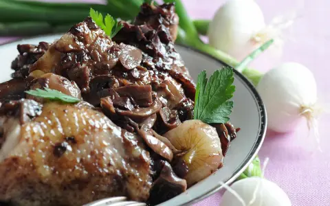 Un plat de coq au vin savoureux, avec des morceaux de poulet tendres, des champignons et des oignons dans une sauce riche.