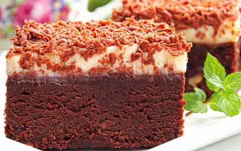 Pyszny torcik brownie z kremową warstwą i posypką czekoladową, ozdobiony listkami mięty.