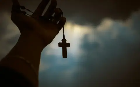 Dłoń trzyma paciorki różańca z krzyżem, symbolizując poszukiwanie prawdy w obliczu niepewności, jak agnostycyzm.