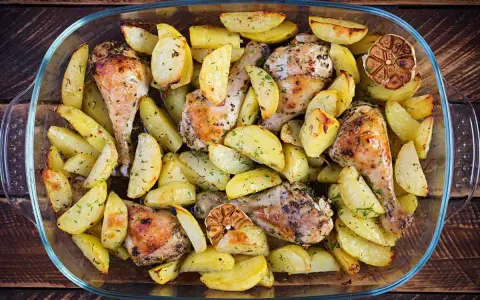 Delizioso pollo al forno con patate, erbe aromatiche e spicchi d'aglio arrostiti, servito in una teglia di vetro.