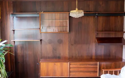En väggmonterad hylla i teak, troligen designad av Poul Cadovius, med glasmonter, lådor och hyllplan.