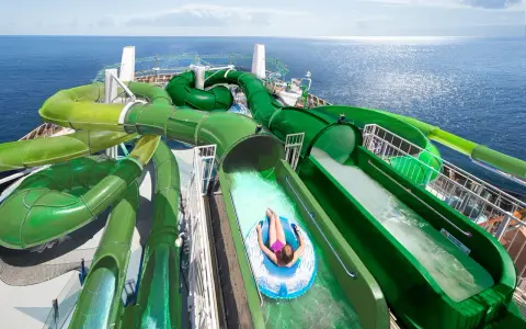 Divertente crociera per bambini con scivoli acquatici verdi che si snodano sul ponte di una nave da crociera, con il mare blu sullo sfondo.