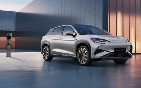 Srebrny SUV BYD Seal U stoi obok ładowarki na tle nowoczesnego budynku.