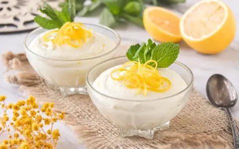 Dos copas de cremoso mousse de limón con leche condensada, decoradas con ralladura de limón y menta.