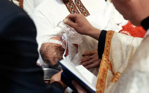 Ceremonia chrztu dziecka. Duchowny polewa główkę niemowlęcia wodą święconą. Warto wiedzieć, ile kosztuje chrzest.