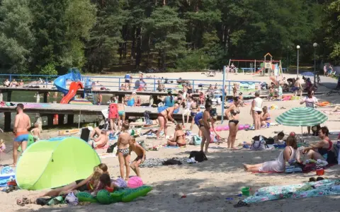 Tłoczna plaża nad jednym z **jezior blisko Wrocławia**. Ludzie opalają się, kąpią i odpoczywają na piasku.