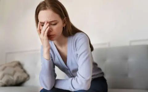 En kvinna sitter på en soffa med handen mot pannan, uttrycker smärta och utmattning i akut fas.