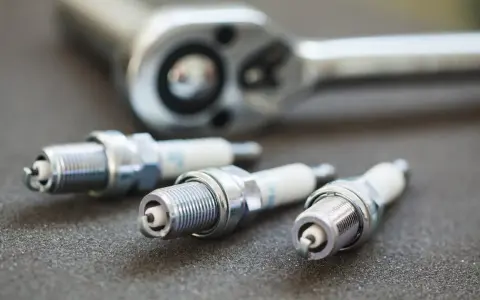 Three spark plugs and a ratchet are laid out, ready for a tune-up. The image highlights the importance of knowing the correct spark plug socket size for the job.