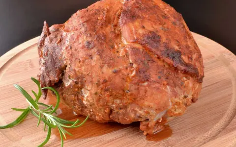 Pieczona szynka z ziołami, która wygląda jakby była przygotowana z użyciem marynaty do szynki. Gałązka rozmarynu dodaje aromatu.