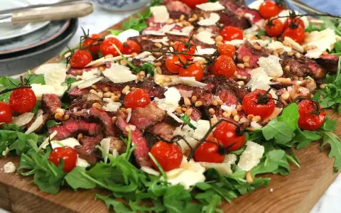 En läcker biff tagliata med körsbärstomater, pinjenötter och parmesan på en bädd av rucola.