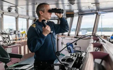 Un officier de marine, comment s'appelle la personne qui conduit un bateau, utilise des jumelles et un téléphone dans la passerelle.