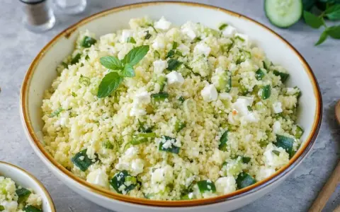 Frischer Couscous-Salat mit Gurkenwürfeln, Feta und Minze, garniert mit einer Minz-Dolde.