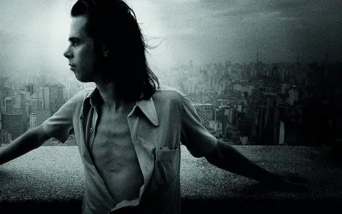 Młody Nick Cave, z rozwianymi włosami, spogląda na miasto. Jego muzyka, jak ten widok, pełna jest mroku i piękna.
