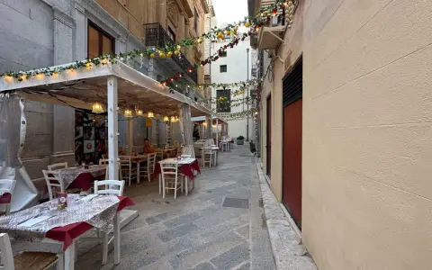 Urocza uliczka w Trapani, gdzie zjeść? Stoliki restauracyjne pod girlandami z cytryn i lampek, idealne na wieczorny posiłek.