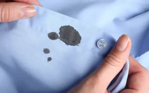 Manos sostienen camisa azul con manchas de bolígrafo. Aprende como quitar manchas de bolígrafo en ropa.