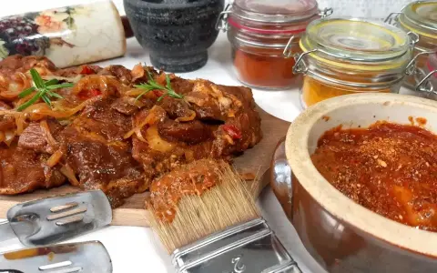 Karkówka na grilla w aromatycznej marynacie, gotowa do pieczenia. Obok pędzel z marynatą i słoiczki z przyprawami.