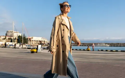Una chica con estilo, con un look clean girl, pasea por el puerto con un abrigo beige y vaqueros anchos.