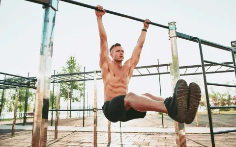 Uomo muscoloso esegue un esercizio di calisthenics per principianti alla sbarra, sollevando le gambe.