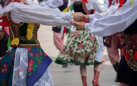 Tancerze w barwnych strojach ludowych, żywa muzyka folkowa w tle.