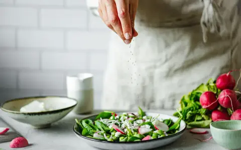 Une main saupoudre des graines sur une salade fraîche. Une idée pour une recette de radis noir.
