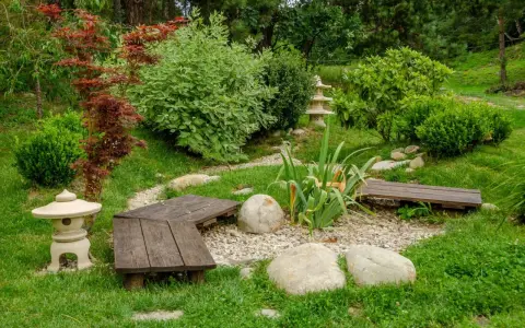 Un paisible petit jardin japonais avec des lanternes, des bancs en bois, des rochers et une végétation luxuriante.