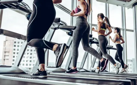 Kobiety ćwiczą cardio na bieżni, biegnąc w siłowni z widokiem na miasto.